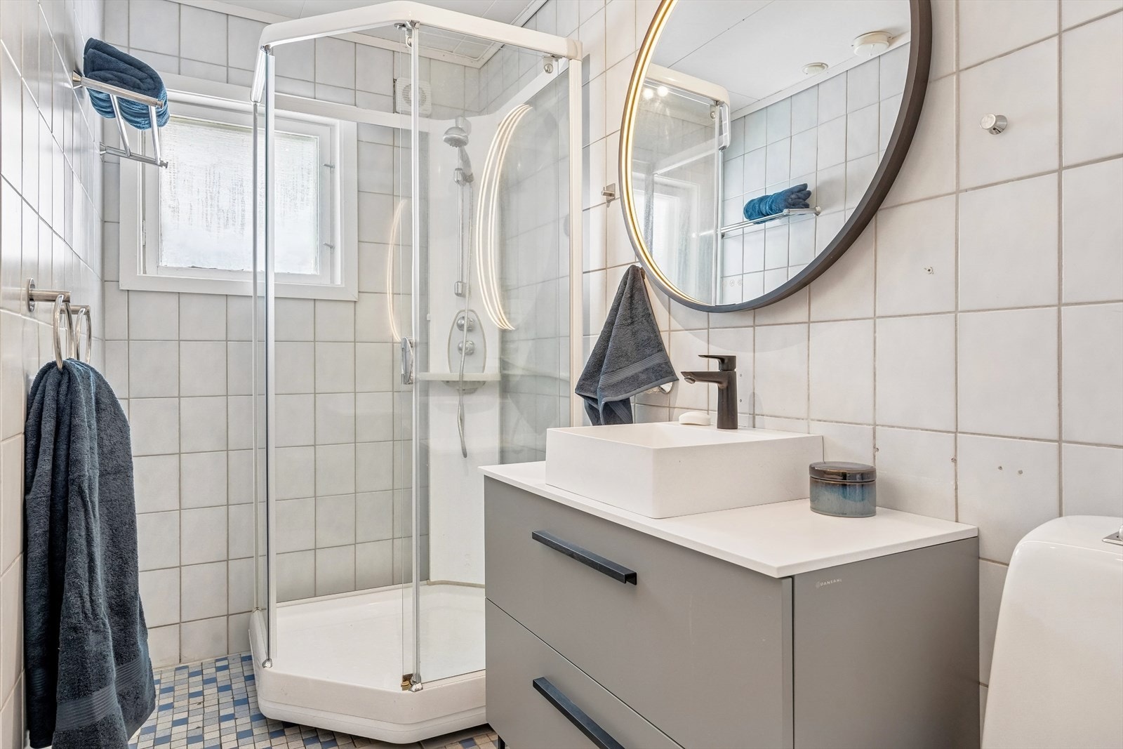 På badet er det flislagte vegger og flislagt gulv. Badet er fra byggeår og inneholder frittstående dusjkabinett, servantskap og toalett. Galleribilde