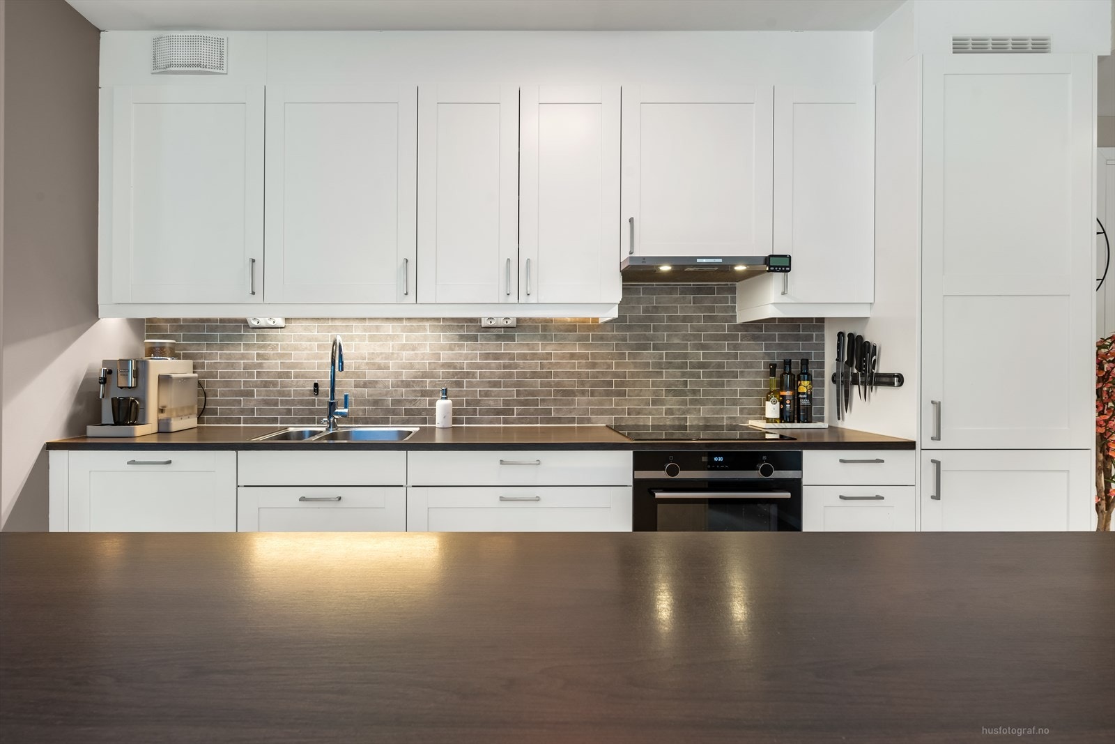 Kjøkkeninnredningen består av induksjonstopp, stekeovn, oppvaskmaskin, kjøl/fryseskap. Det er montert lekkasjevarsler i kjøkkenbenk og det er komfyrvakt., fliser over benk, belysning under overskap og ventilator. Galleribilde