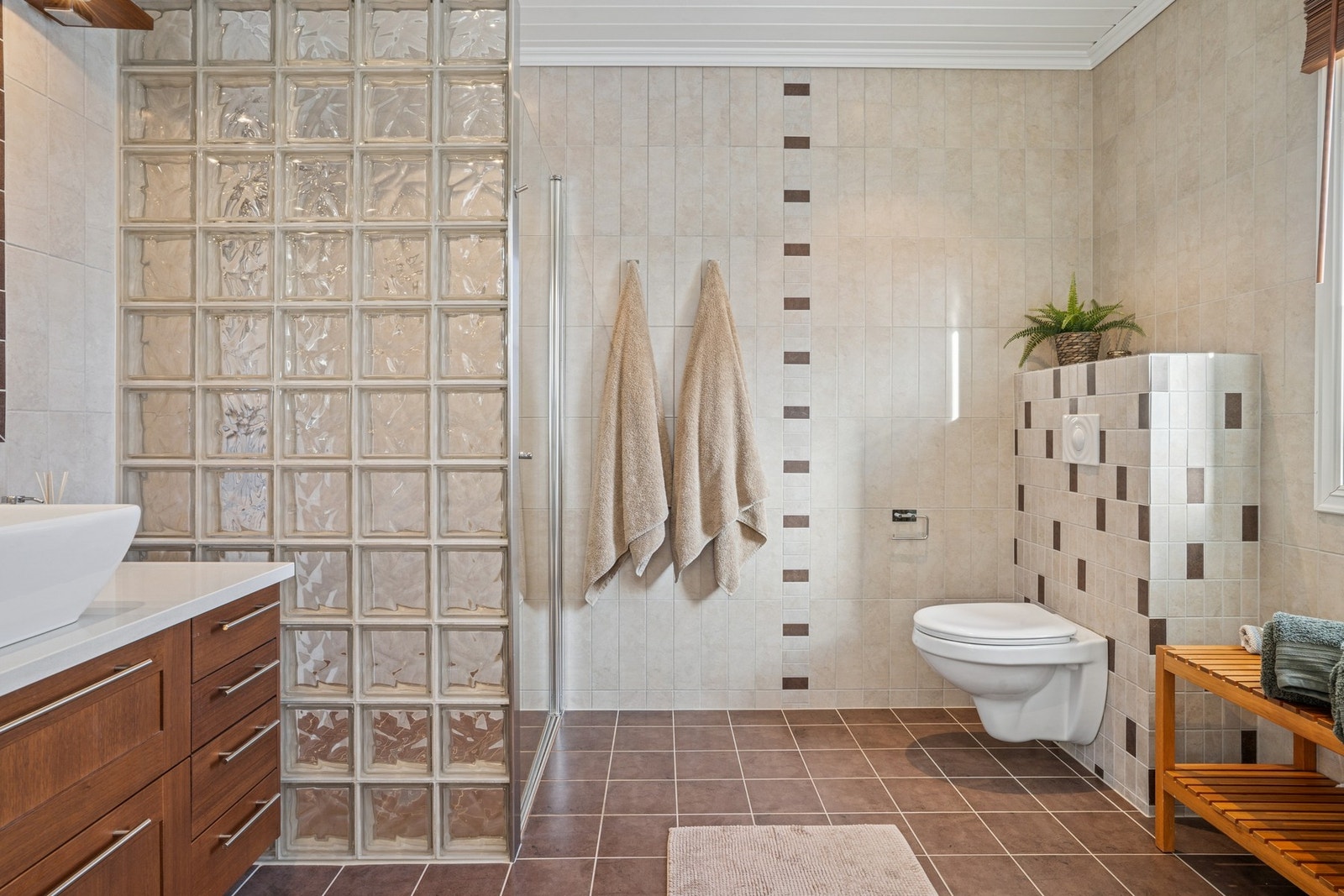 Dette er et flislagt baderom, utstyrt med gulvvarme, vegghengt servantinnredning, dusjnisje og toalett. Galleribilde