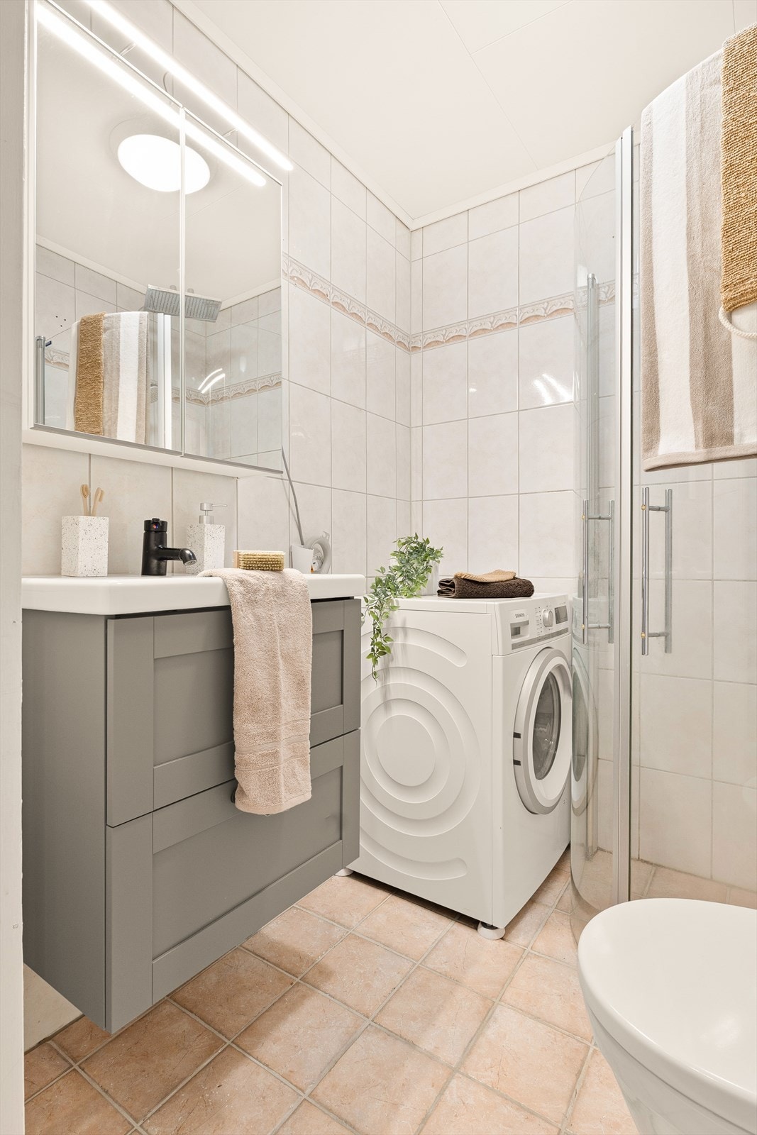 Baderomsinnredningen består av dusjdører, servant med møblement, wc og opplegg for vaskemaskin. Galleribilde