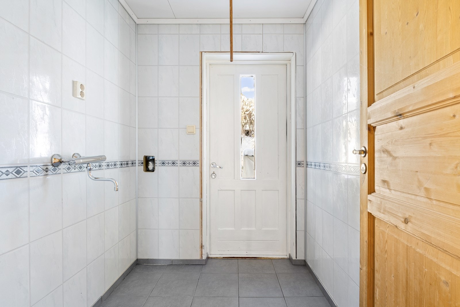 Vaskerommet har fliser på gulv og våtromsplater på veggene, samt opplegg for vaskemaskin. Fra rommet er det direkte utgang til husets bakside. Galleribilde