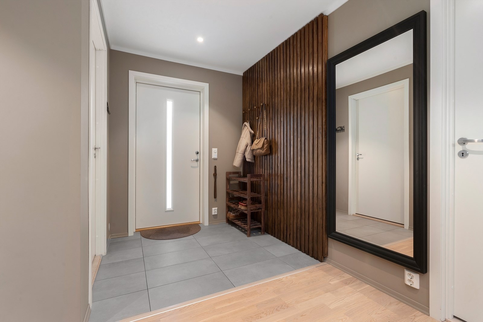 Entréen har en moderne og innbydende stil med en markant spilevegg med oppheng for yttertøy, som tilfører varme og uttrykk. Store fliser ved inngangspartiet. Galleribilde