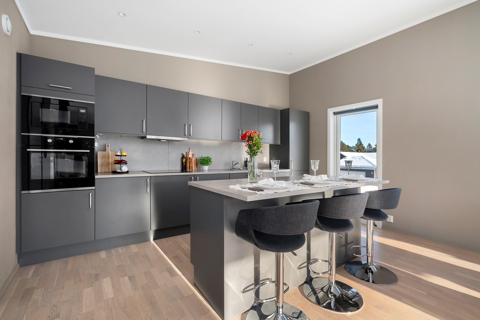 Delikat kjøkkeninnredning med slette, grå fronter og benkeplate av laminat med stålkum, som bærer et harmonisk samspill mellom eleganse og funksjonalitet. Galleribilde