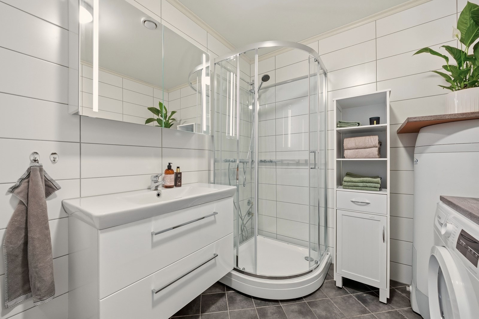 Badet er utstyrt med heldekkende servant med underskap, speilskap, dusjkabinett og toalett, samt nisje for vaskemaskin og tørketrommel Galleribilde