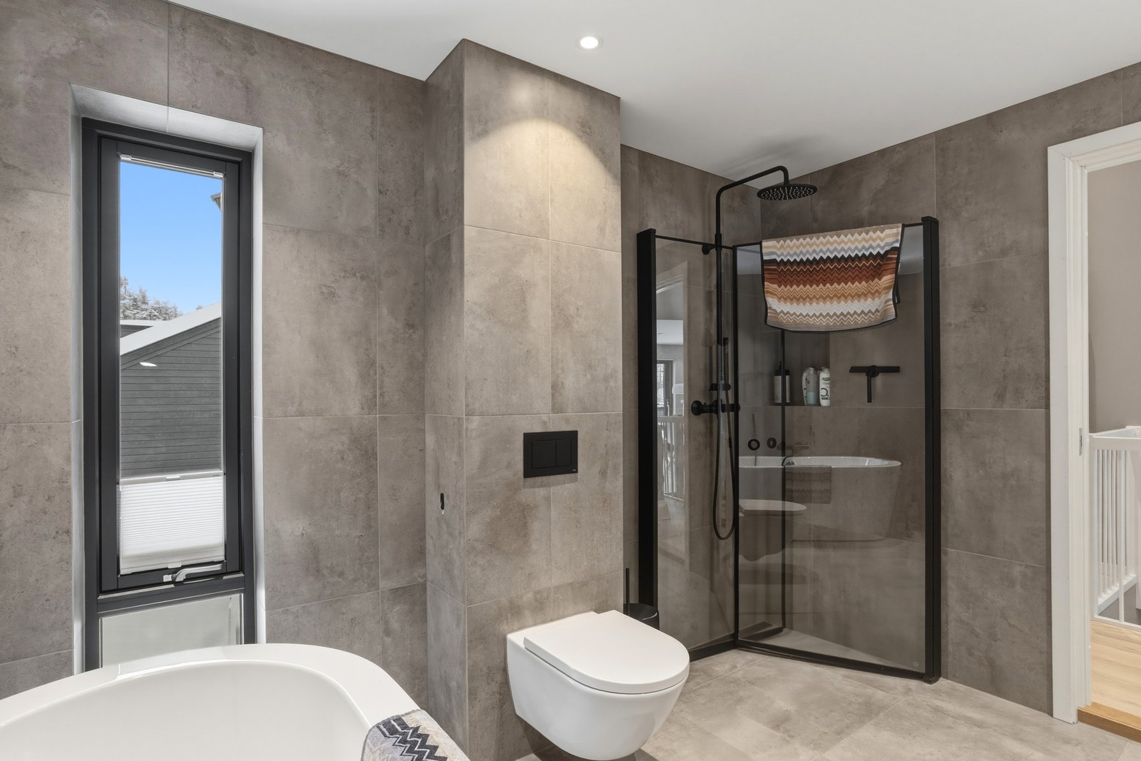 Badet har innredning med ett-greps blandebatteri og speil på vegg, vegghengt toalett, badekar og dusjhjørne med innfellbare glassdører Galleribilde