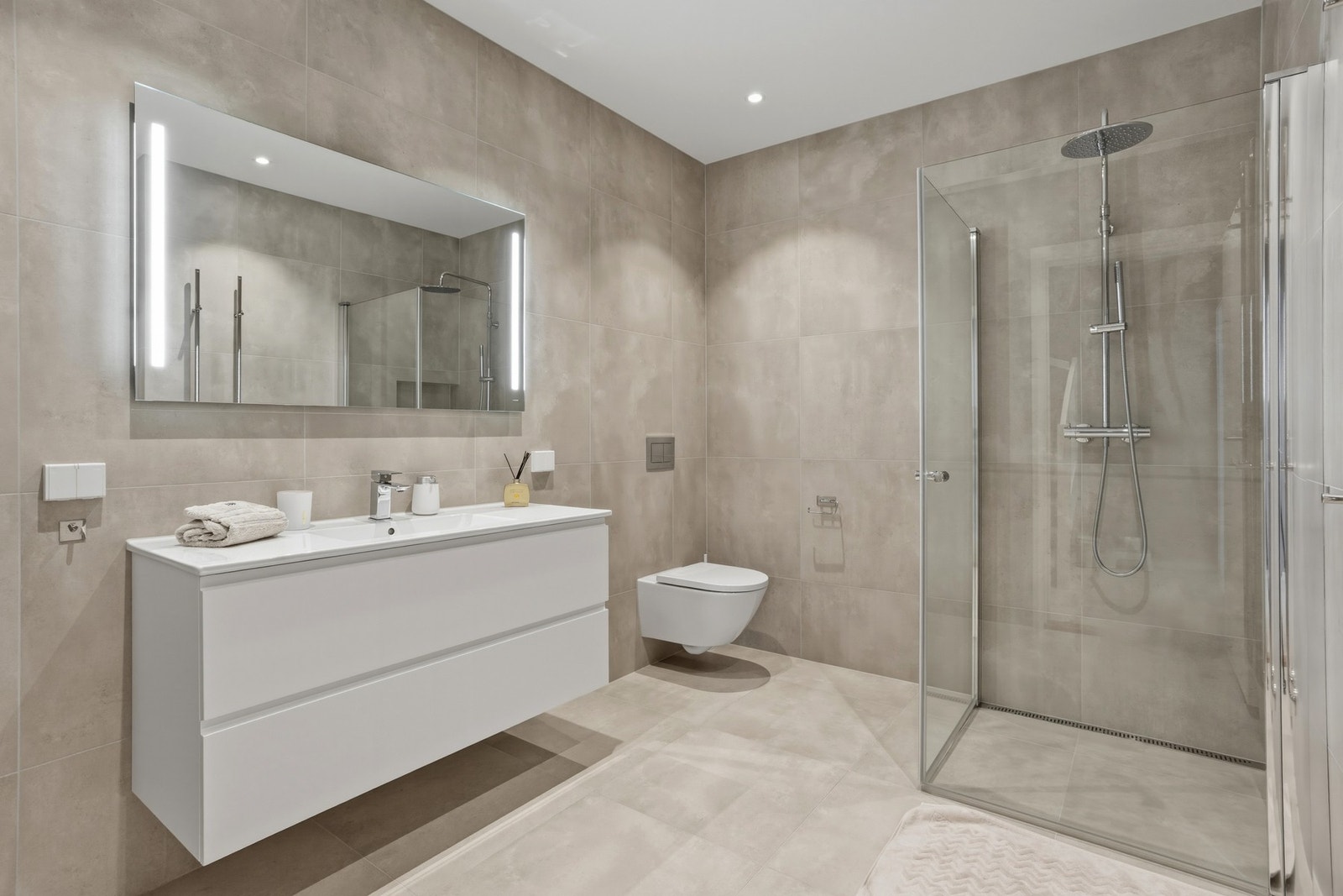 Delikat, helfliset bad innredet med vegghengt toalett, servantinnredning med armatur og speil på vegg, samt dusjhjørne med innfellbare glassdører Galleribilde