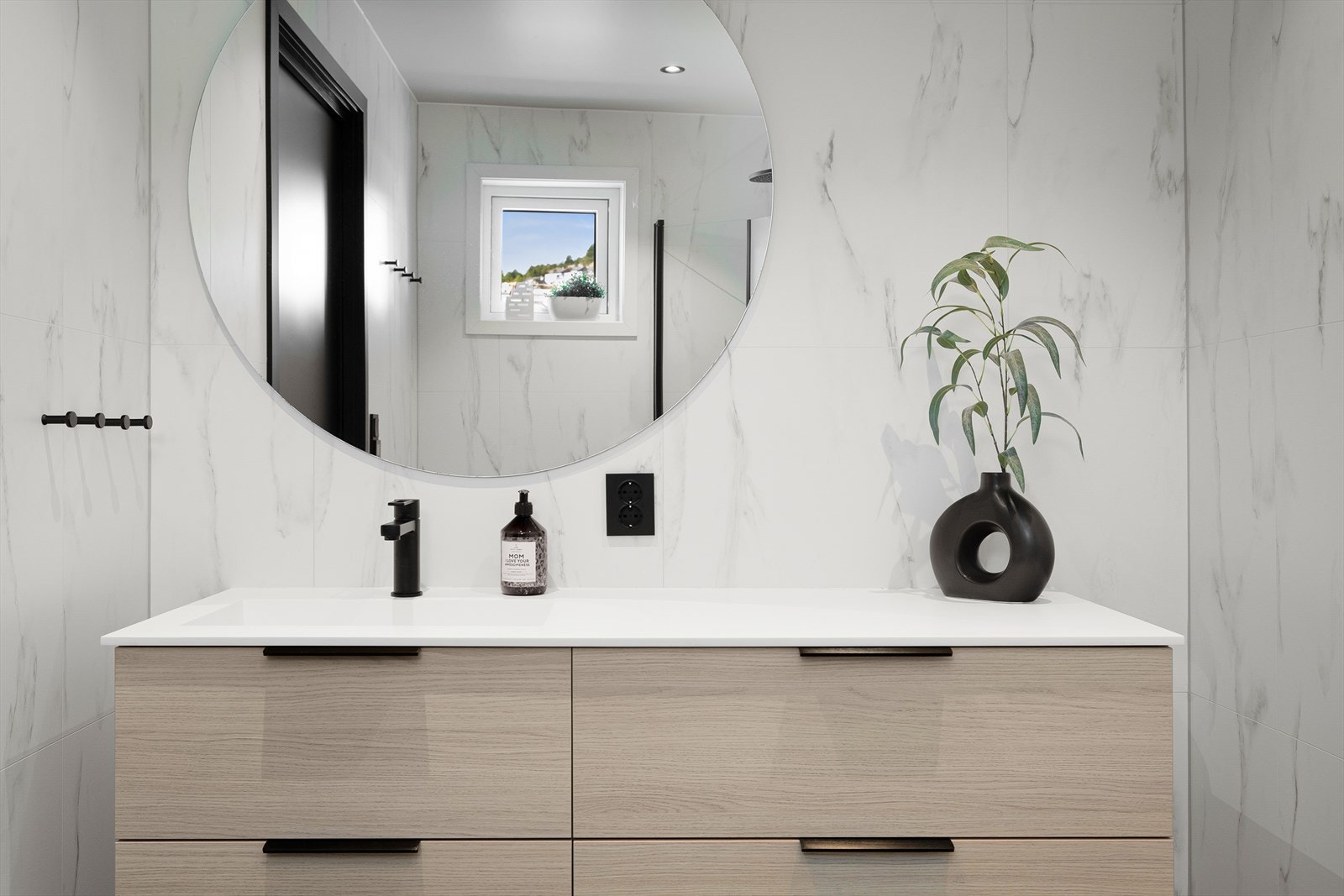 Rommet er flott innreidd med nedfelt servant, veggmontert toalett og takdusj. Svarte detaljar gir eit moderne og stilreint uttrykk som hevar heilskapen til resten av leilegheita. Galleribilde