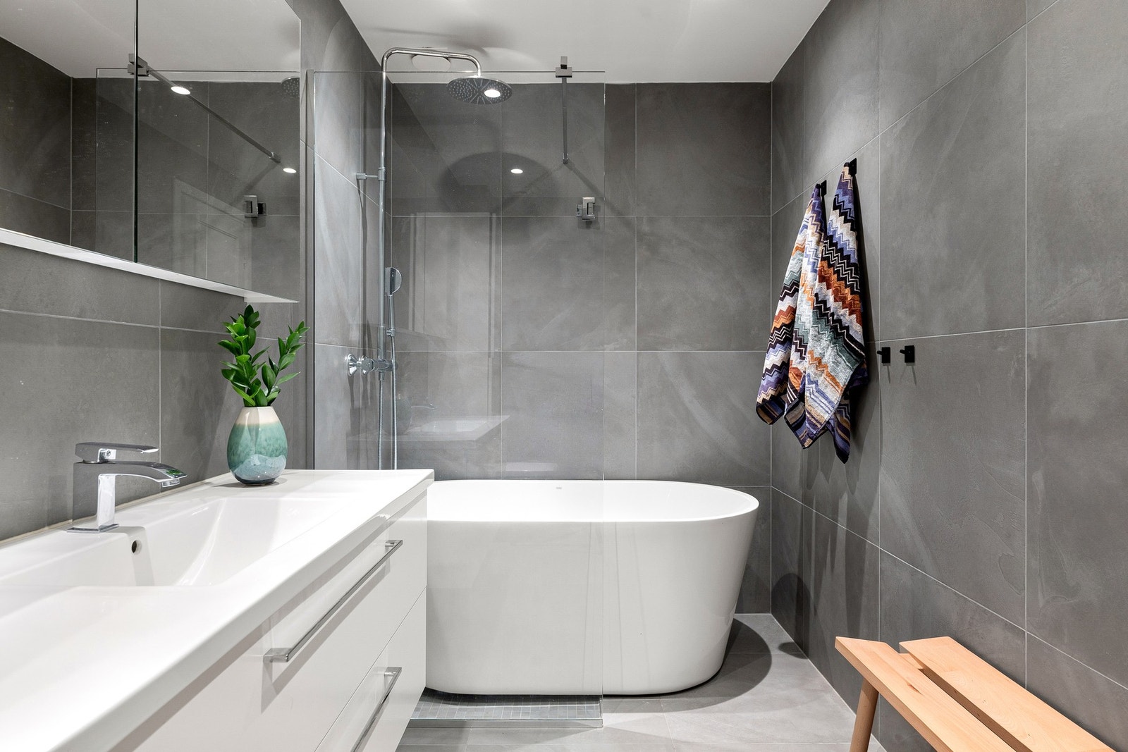 Romslig og delikat baderom med frittstående badekar og dusj med regnfallsdusj bak glassvegg. Store fliser gir et helhetlig og moderne uttrykk. Galleribilde