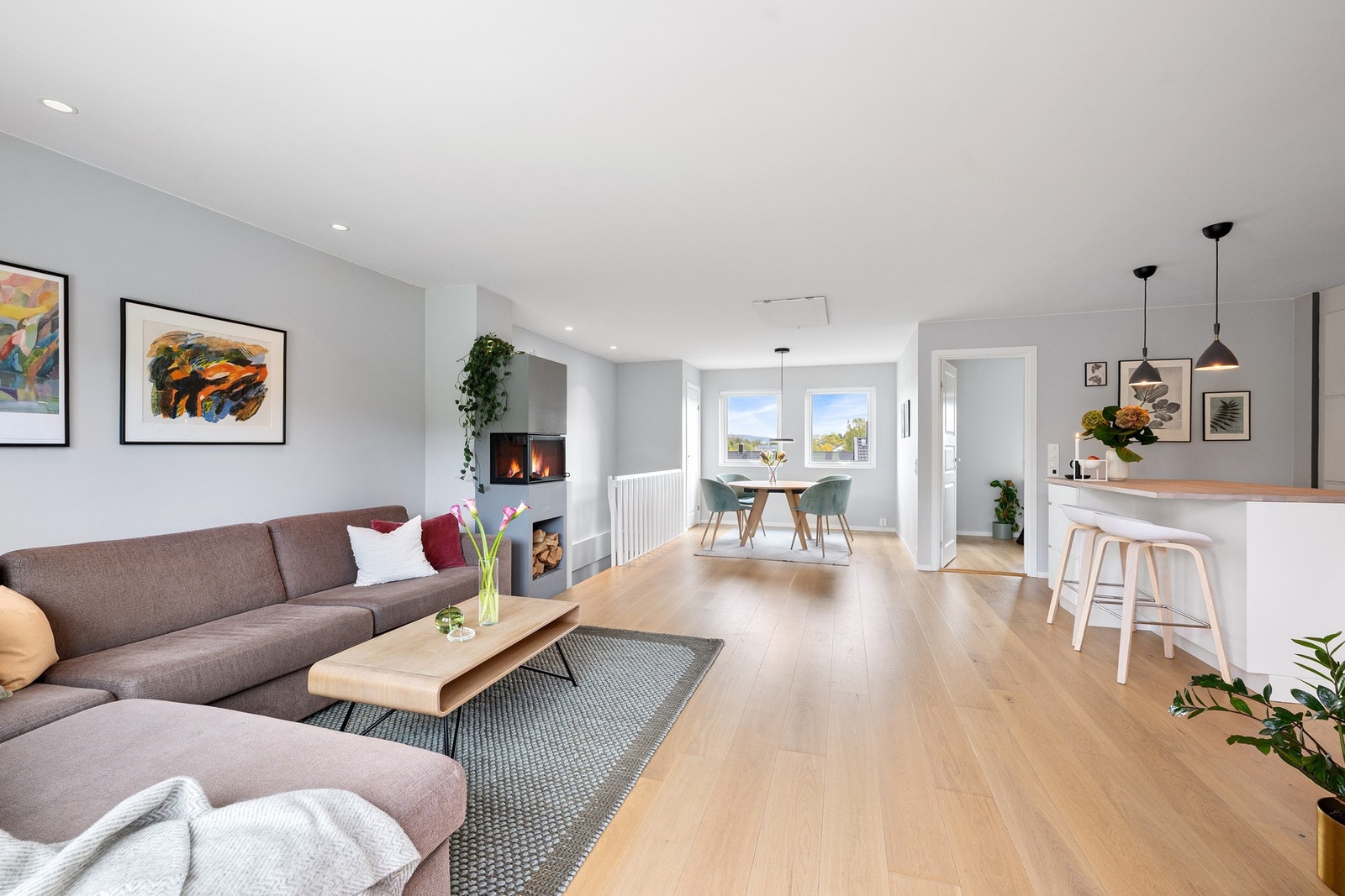 Oppholdsrommet har rikelig med naturlig lys og et kjøkken i åpen løsning mot spiseplass og stue, noe som gir en luftig og sosial romfølelse. Galleribilde