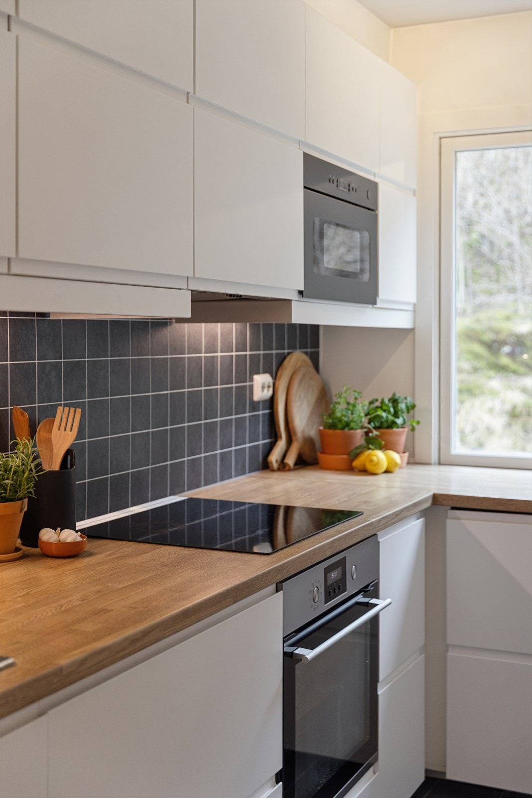 Innredningen har hvite, glatte fronter, laminert benkeplate og kitchenboard mellom benk og overskap. Galleribilde