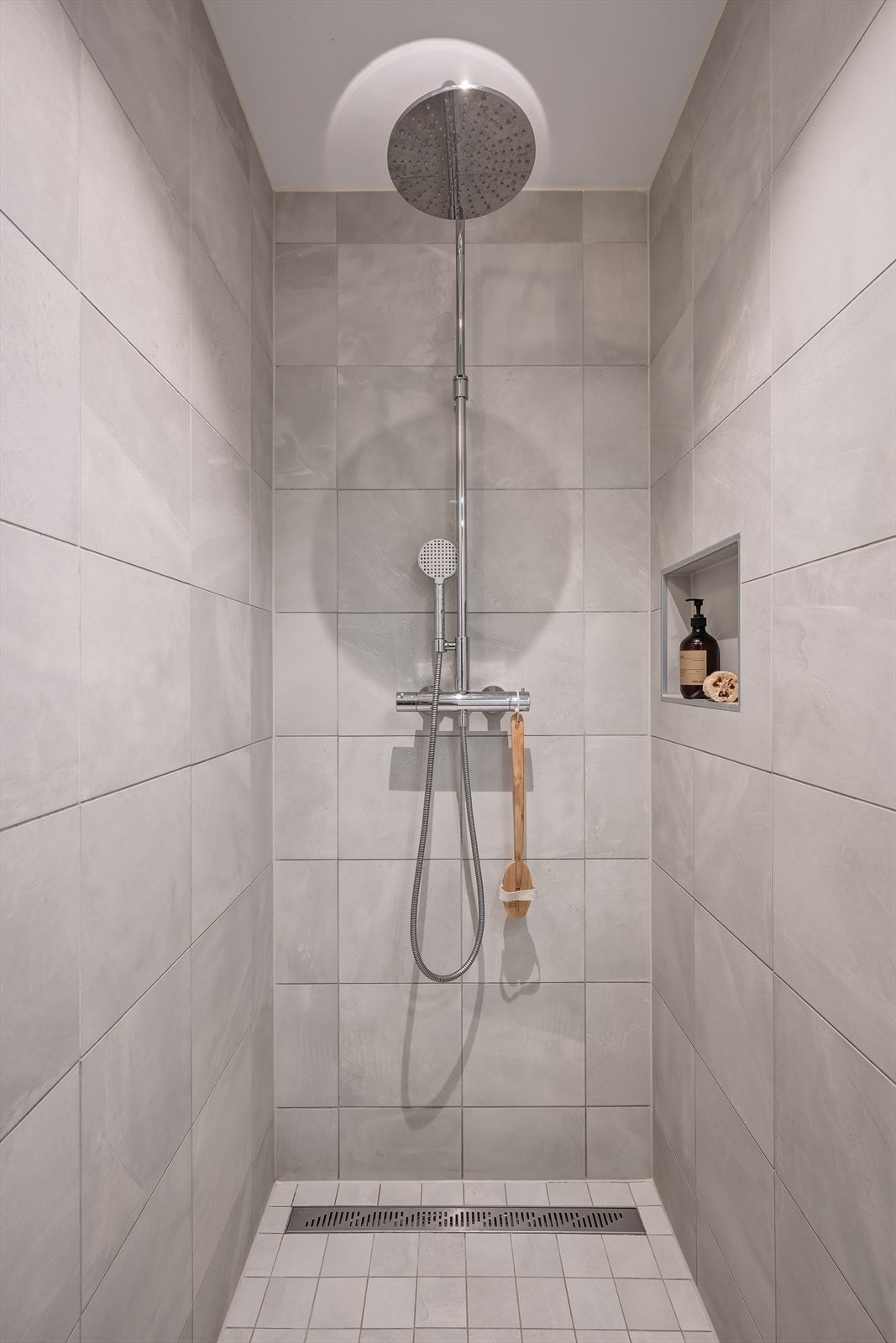 Badet er utstyrt med vegghengt toalett, dusjsoneløsning direkte på gulv, og en servantinnredning med skuffer. Galleribilde