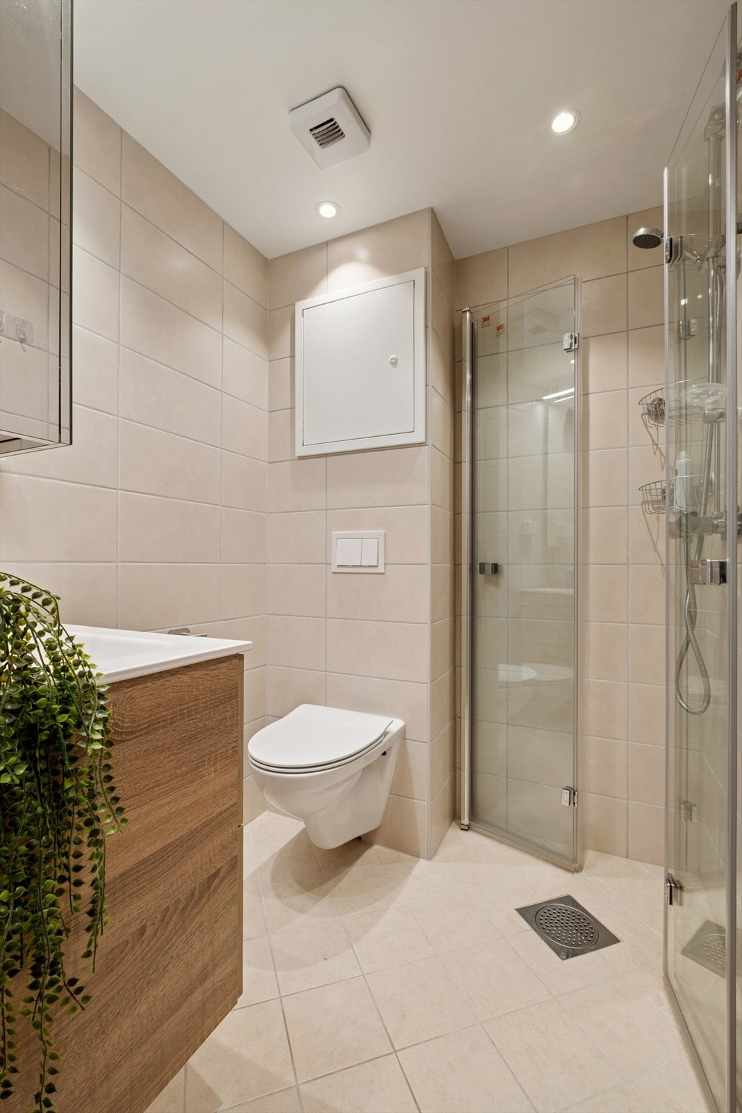 Pent og moderne, flislagt bad med vegghengt toalett, praktiske og plassbesparende dusjløsning og servantskap med speil Galleribilde