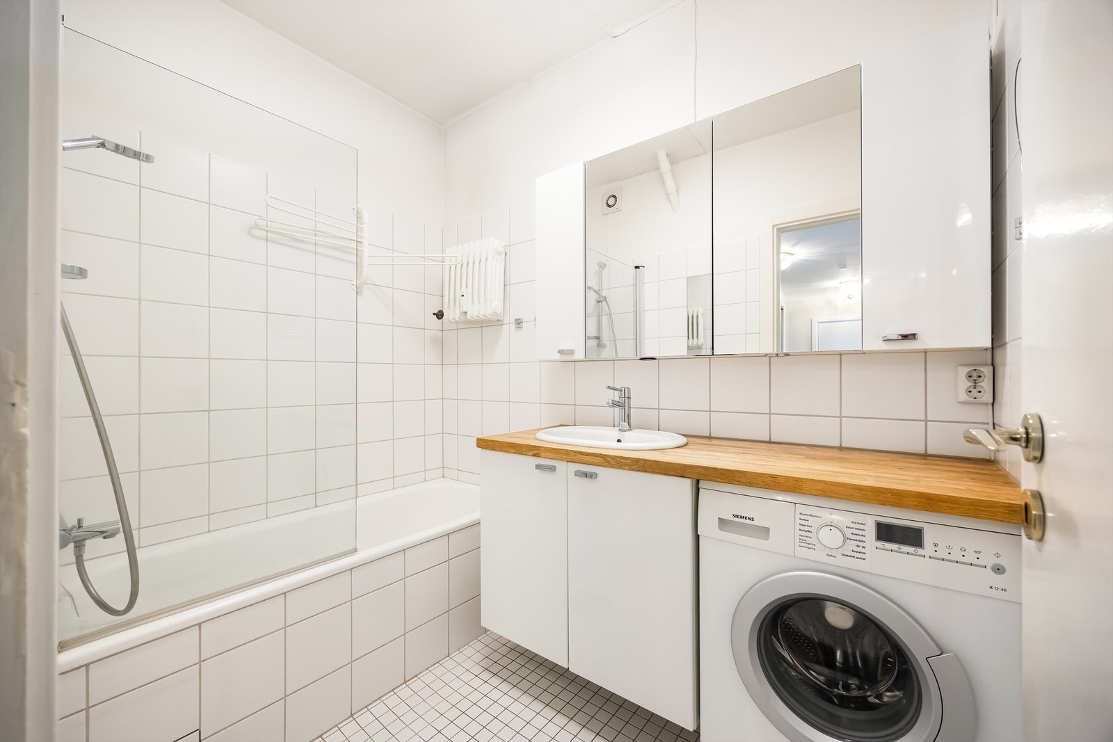 Lyst bad som er innredet med vegghengt servant med benkeplate i heltre og nedfelt vask. Innbygget badekar med glassvegg og dusjarmatur. Galleribilde