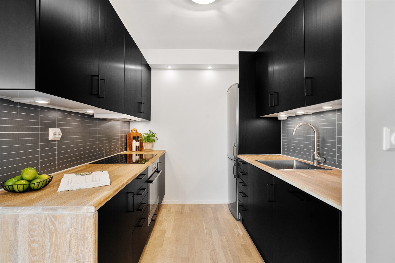 Flott kjøkken med svarte, slette fronter og rikelig med skap- og benkplass. Frontene er folierte og benkeplaten er av tre. Galleribilde