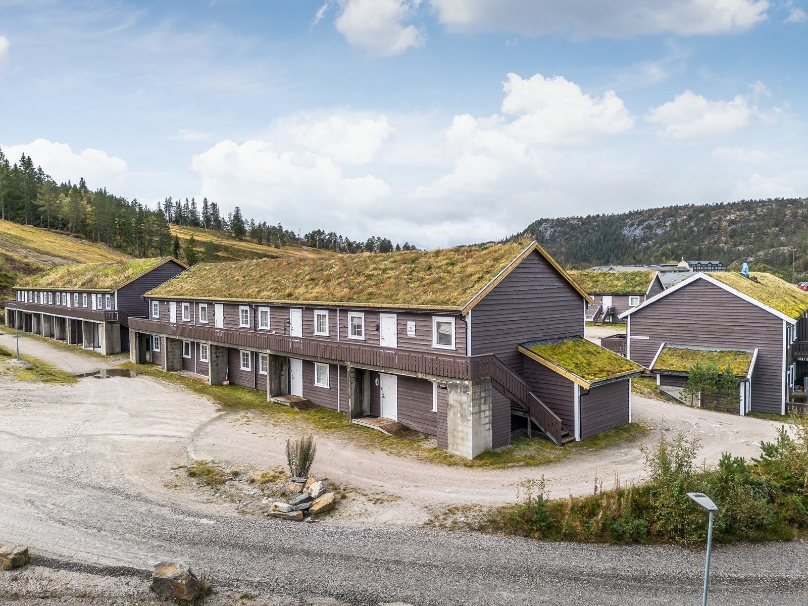 Tomten er opparbeidet med gruset innkjørsel og stor gårdsplass. Det er kjørevei frem til inngangsdøra for av- og pålessing, hvor denne leiligheten ligger lettvint til i 1. etasje i den ene enden av bygget. Galleribilde