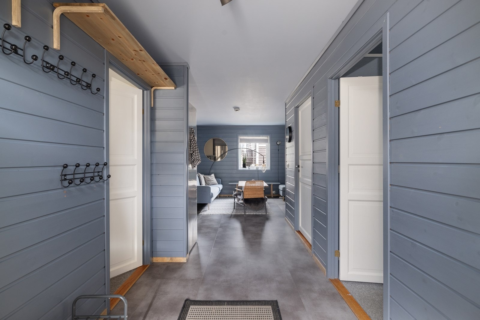 Innbydende gang med blåmalte panelvegger og moderne detaljer, som leder inn til en koselig og stilfull stue og kjøkken. Galleribilde