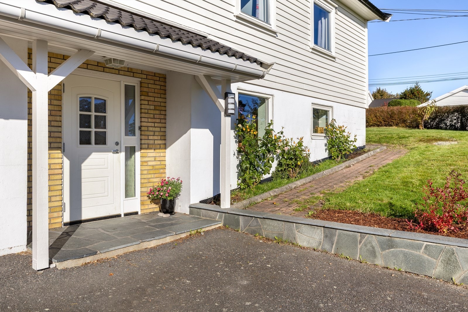 Overbygget inngangsparti med fine forstøtningsmurer og blomsterbed. asfaltert oppkjørsel. Galleribilde