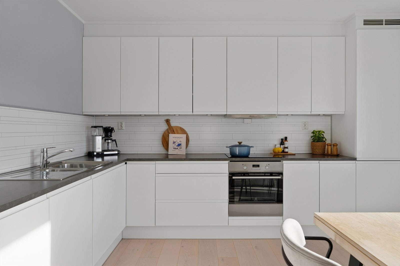 Kjøkkenet fremstår både funksjonelt og tidløst, med glatte fronter, laminert benkeplate og praktiske kitchen board-plater over benk som gjør rengjøringen enkel. Galleribilde