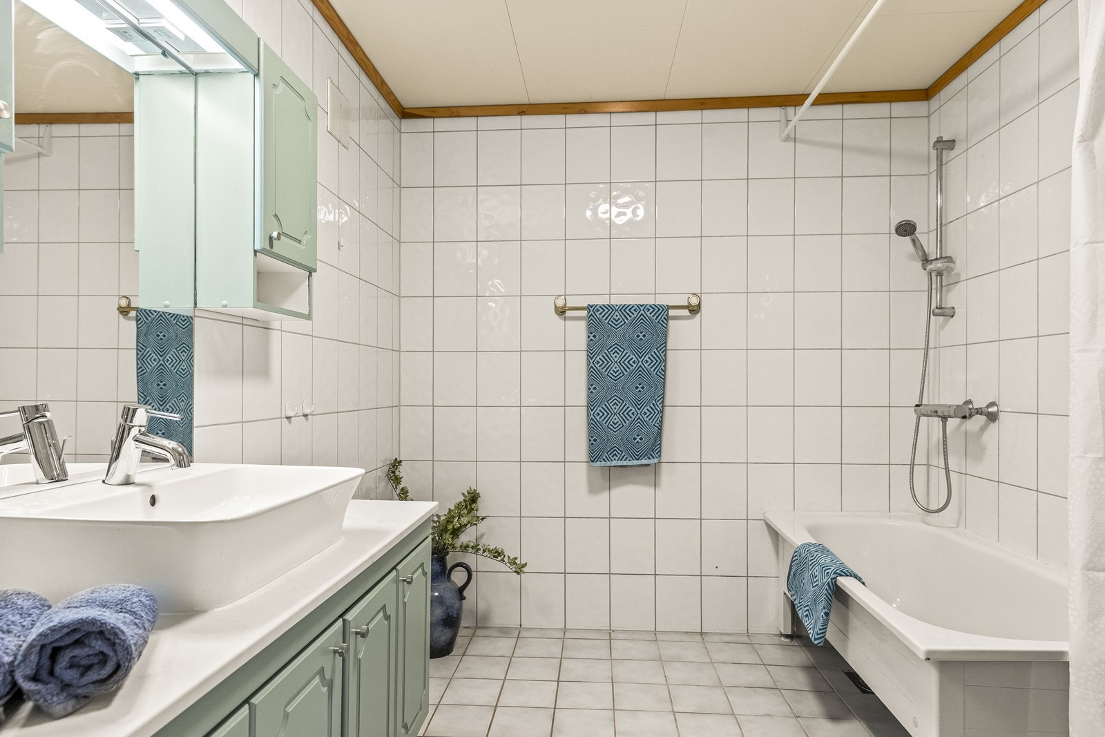 Badet er innredet med en baderomsinnredning i en lys grønntone, med benkeplate, servant og god oppbevaringsplass i skap. Over servanten er det montert speil. Videre er rommet utstyrt med badekar med dusjløsning, samt toalett. Galleribilde