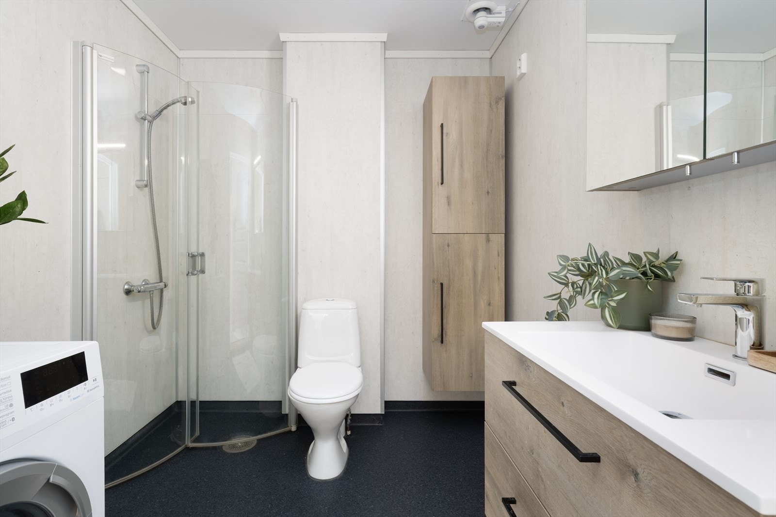 Badet er innredet med toalett, dusjhjørne og servantinnredning med skuffer, skap og speilskap, samt opplegg for vaskemaskin. Badet har våtromsbelegg på gulv med varmekabel og våtromsplater på vegger. Galleribilde