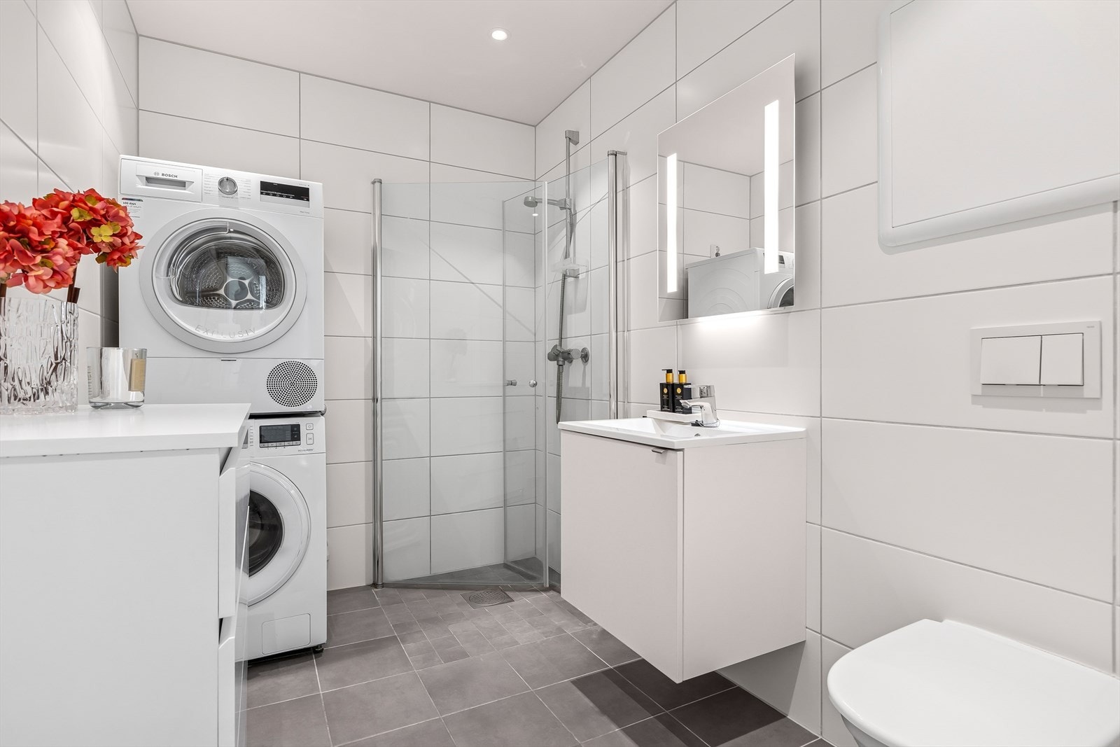 På badet er det flis på gulv og vegg, dusjvegger av glass og dusjgarnityr på vegg. Vegghengt toalett. Innredning med servant og opplegg for vaskemaskin. Galleribilde