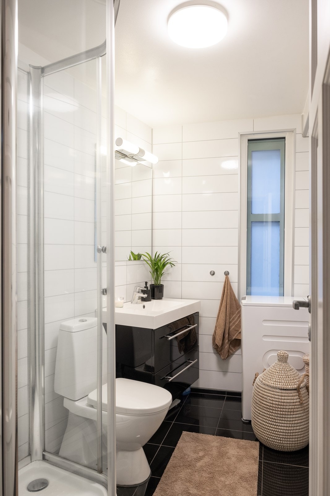 Badet har dusjkabinett, gulvstående toalett, servantskap med speil og opplegg for vaskemaskin. Galleribilde