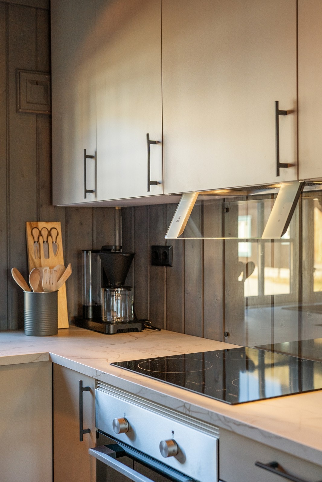 Tilpasset backsplash i glass over platetopp. Det er montert kjøkkenventilator med kullfilter. Galleribilde