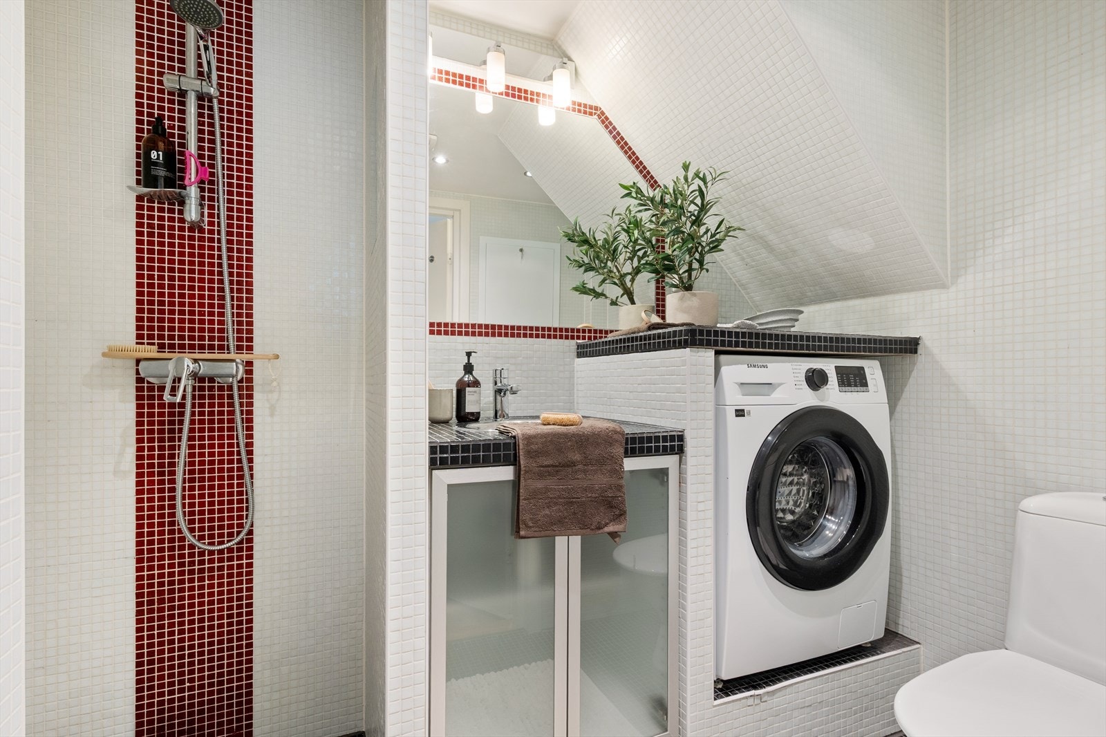 Praktisk helfliset bad utstyrt med servant i møbel, toalett, dusjhjørne og opplegg for vaskemaskin. Galleribilde