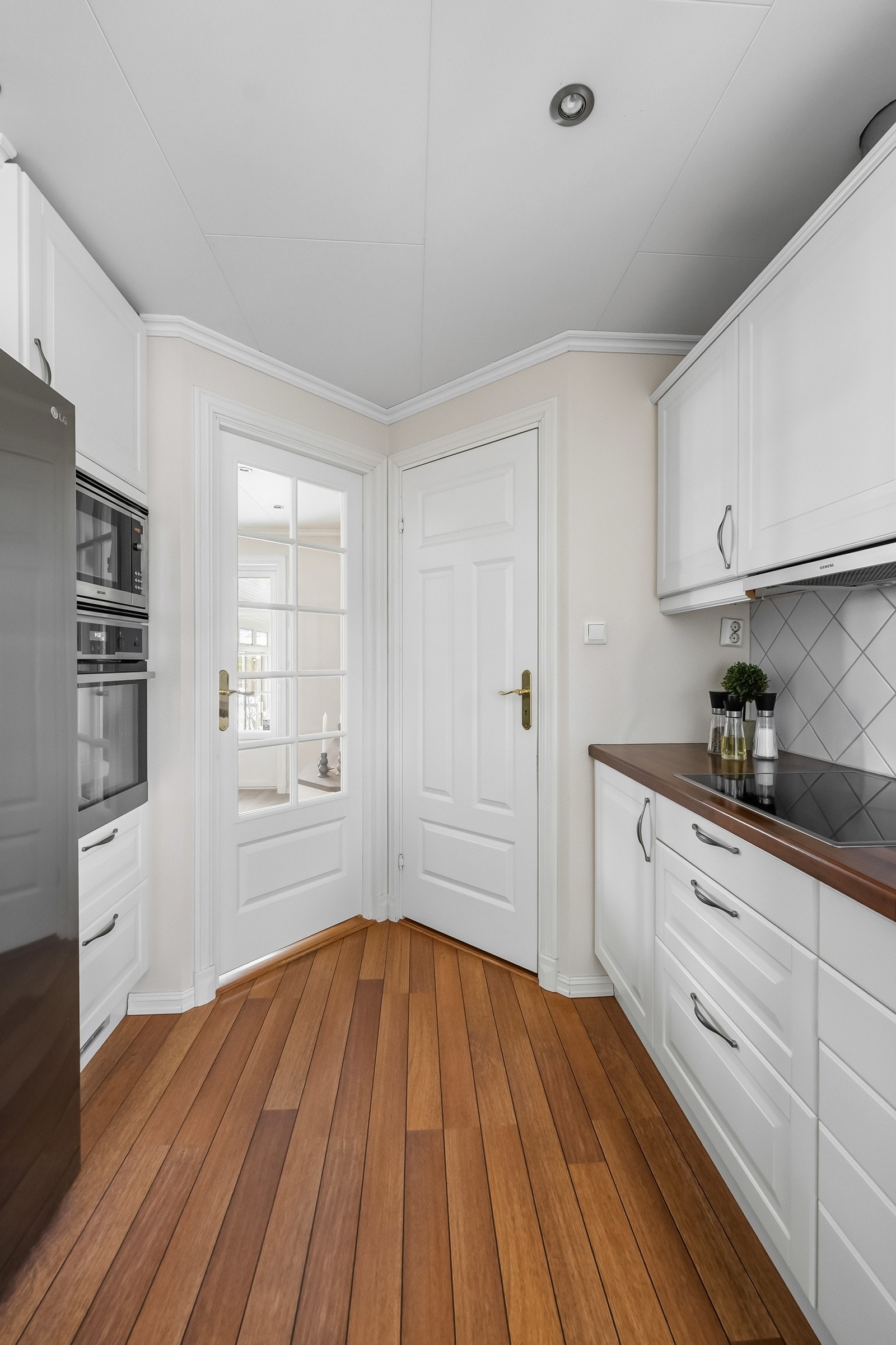 Kjøkkeninnredning med profilerte fronter og enkelte glassfronter i overskap. Dør til venstre er inn til stue. Dør til høyre er inn til bod, hvor ekstra matvarer og kjøkkenutstyr kan oppbevares. Galleribilde