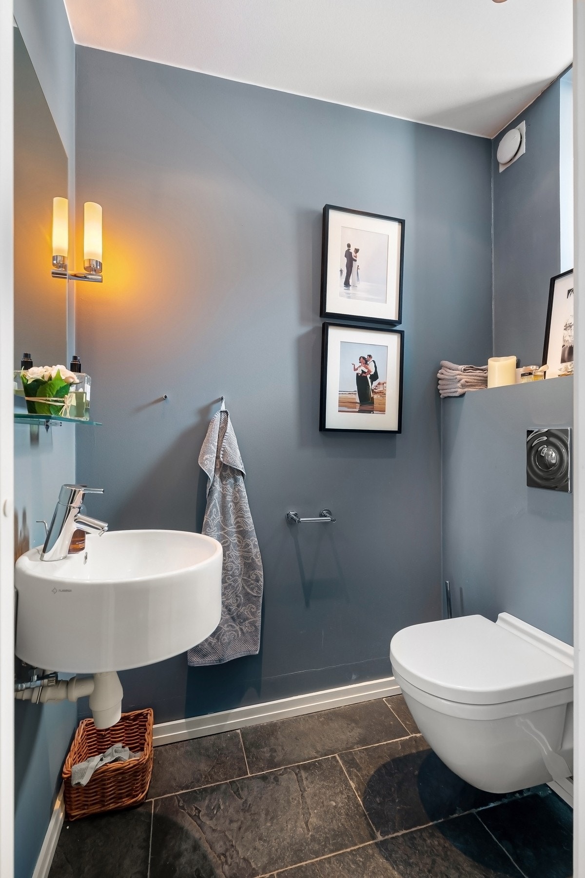 Toalettrom med naturstensgulv med varmekabler og malte veggflater. Rund porselensservant, speil og belysning. Vegghengt toalett. Galleribilde