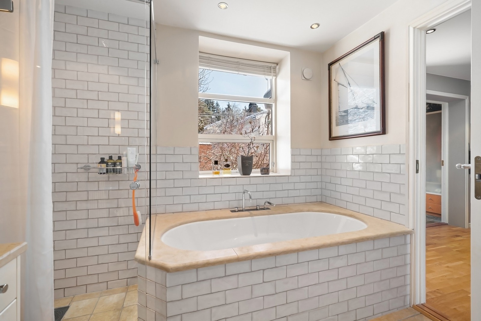 Innbygget flislagt badekar med tilpasset natursten kant rundt kar. Glassvegger rundt dusjsonen. Vegghengt toalett. Galleribilde