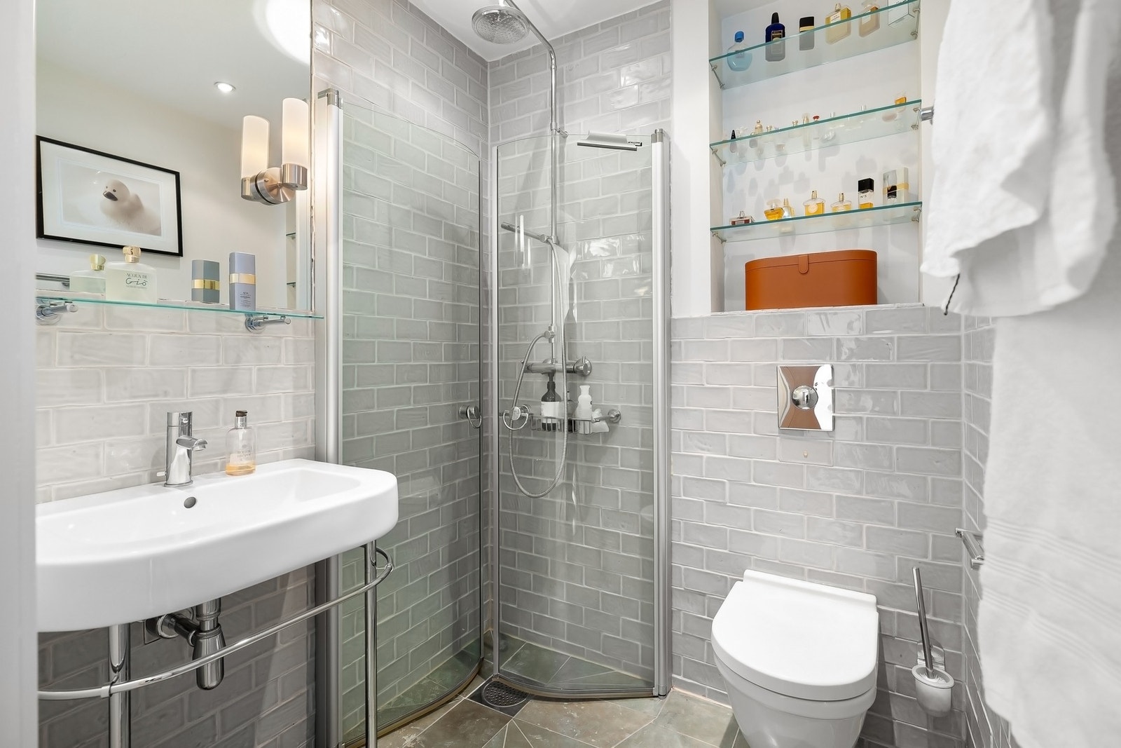 Baderom med flislagt gulv med varmekabler, flislagte vegger i våtsoner og malte flater for øvrig. Porselensservant, speil og belysning, fritthengende dusjvegger og vegghengt toalett. Galleribilde