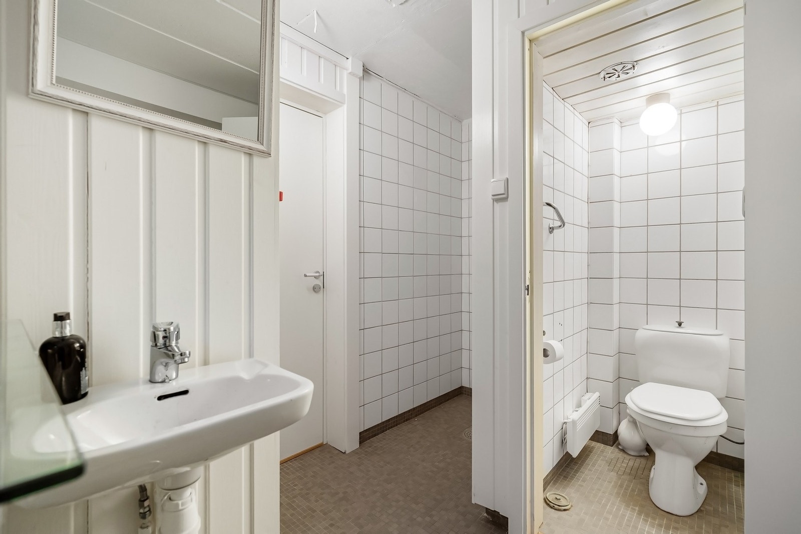 Baderom med flislagt gulv og fliser på vegger i våtsoner, forøvrig malt panel. Porselensservant på vegg, gulvmontert toalett og dusjarmatur. Galleribilde