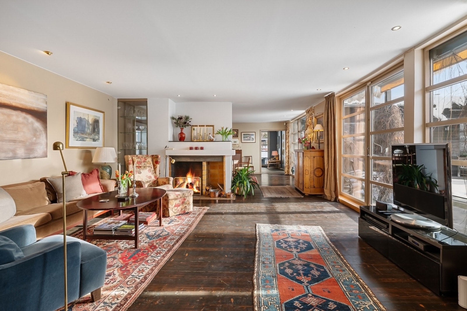 Innbydende stue med stemningsfull peis, rikelig med lys og sømløs overgang til hagearealet. Galleribilde