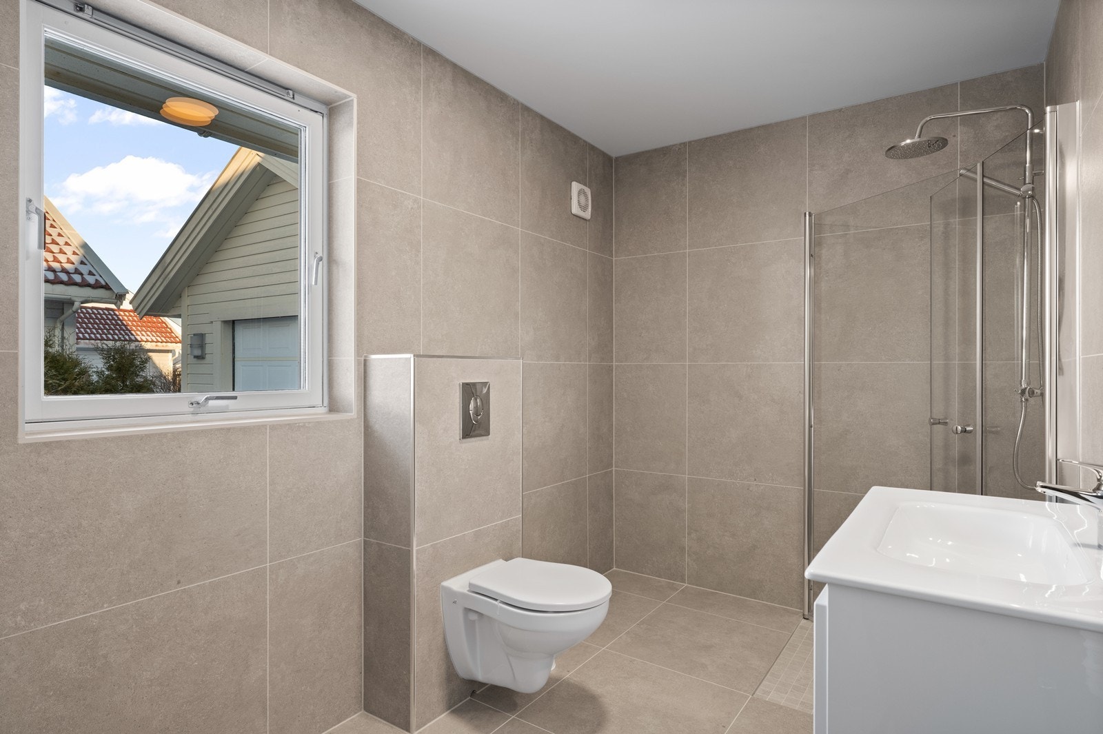 Rommet er utstyrt med veggmontert toalett og praktiske dusjvegger i et hjørne. Galleribilde