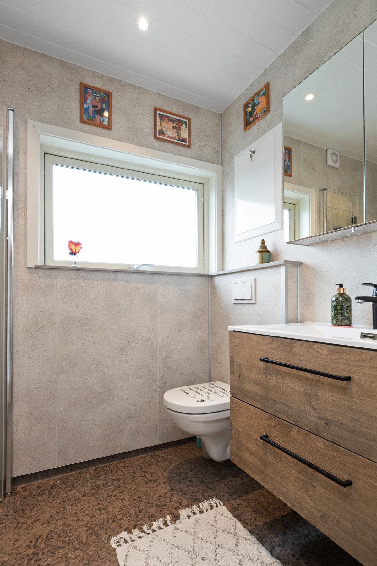 Innredningen består av en heldekkende servant på brun skuffeseksjon, et speilskap, et veggmontert toalett og et dusjhjørne med innfellbare glassdører. Badet har også opplegg for vaskemaskin. Galleribilde