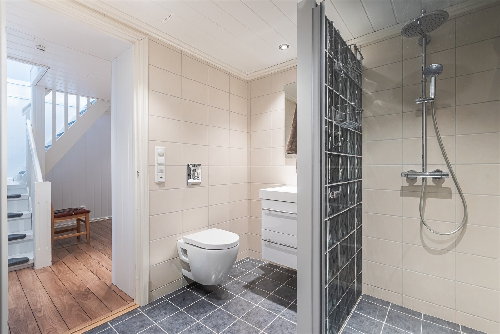 Flislagte vegger og gulv med elektriske varmekabler gir et komfortabelt baderomsmiljø. Dusjhjørne med glassvegg og veggmontert toalett gir moderne sanitærløsning. Galleribilde