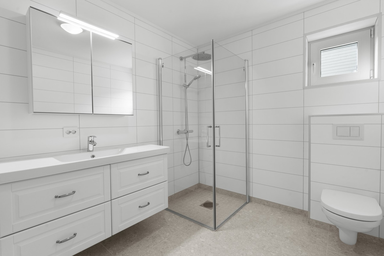 Romslig og lyst bad med dusjhjørne, vegghengt toalett og varmekabler i gulv. Galleribilde