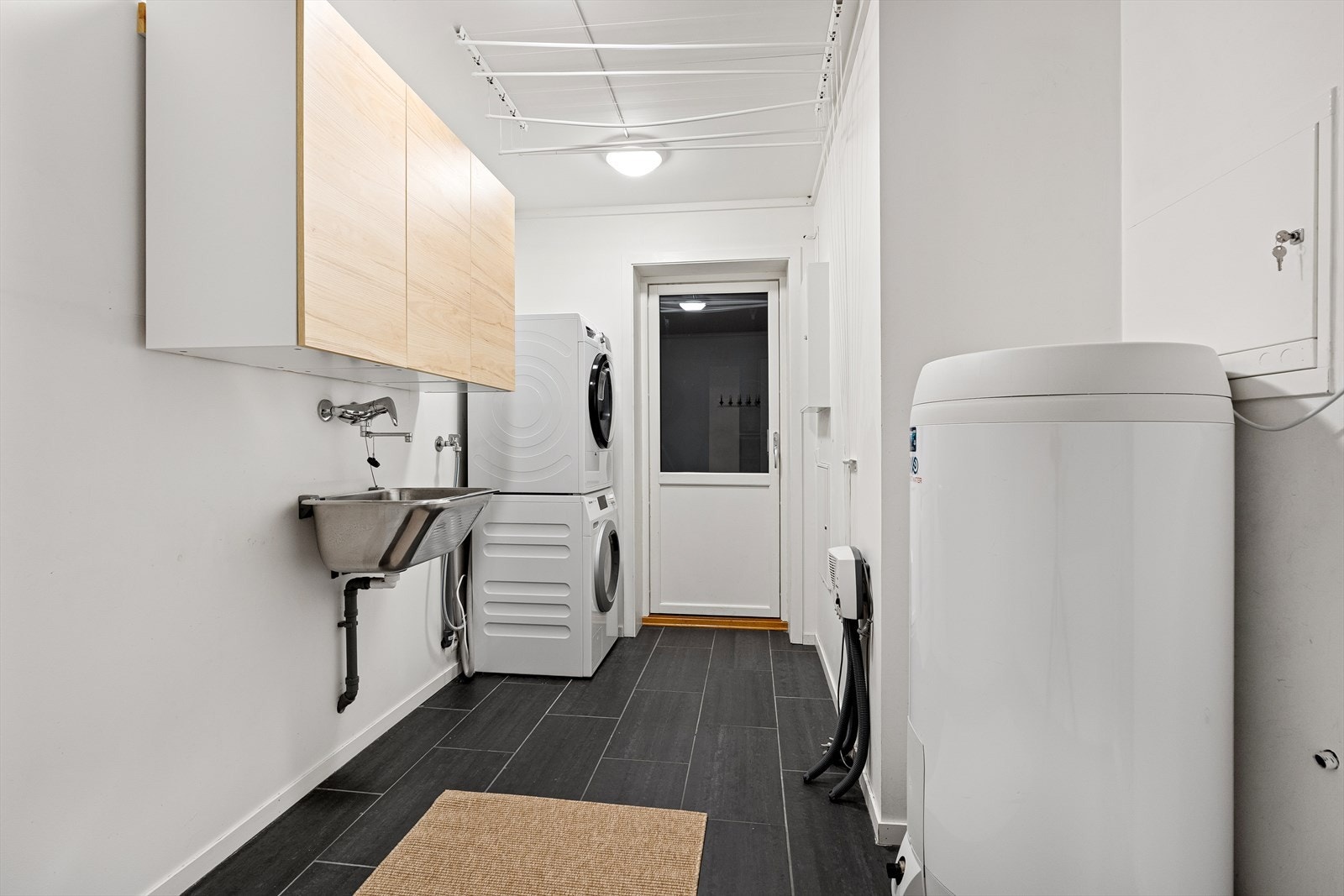 Vegg i vegg med badet finner du et praktisk vaskerom med direkte tilkomst til garasjen. Vaskerommet har fliser på gulvet med varmekabler, samt plass og opplegg for vaskemaskin/tørketrommel, utslagsvask, varmtvannsbereder, samt øvrig oppbevaring. Galleribilde