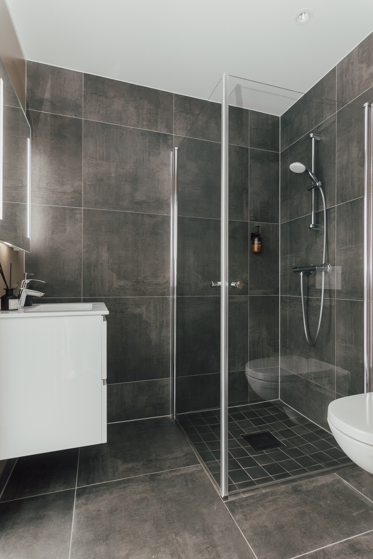 Badet er innredet med vegghengt toalett, servant med innredning og dusjhjørne. Galleribilde