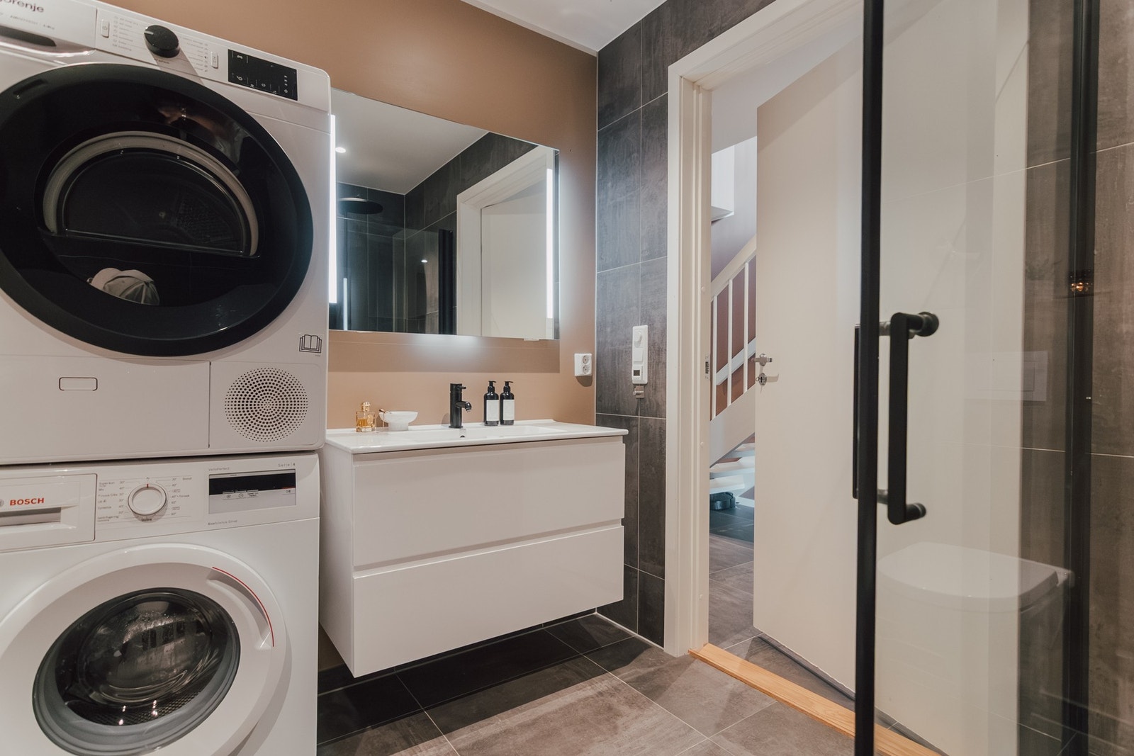 Badet er innredet med vegghengt toalett, servant med innredning, dusjhjørne og opplegg for vaskemaskin. Galleribilde