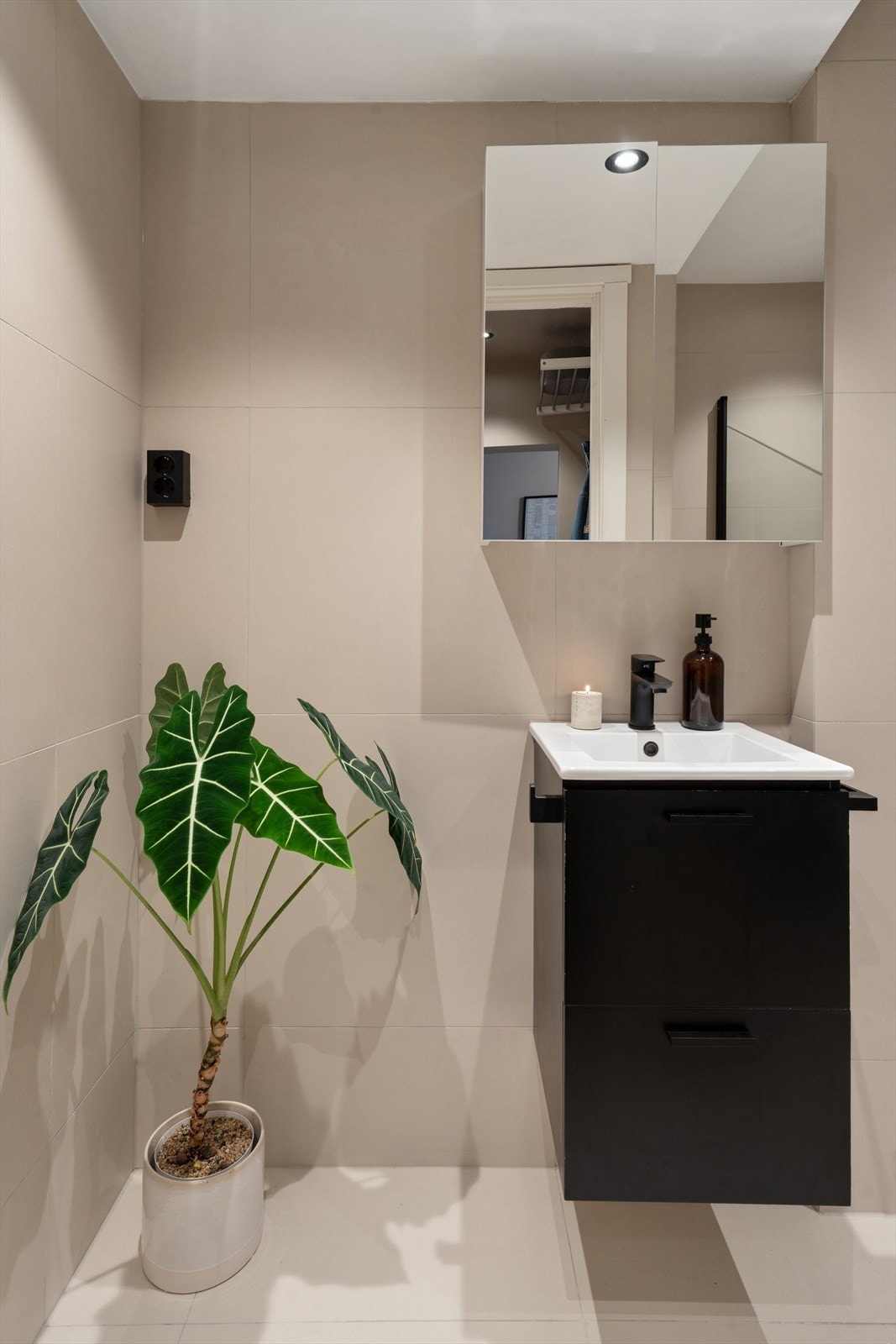 Servant med mørk innredning og ettgreps armatur, samt speilskap med oppbevaringsmuligheter. Flislagte overflater og downlights i himling gir et helhetlig og tidsriktig preg. Galleribilde