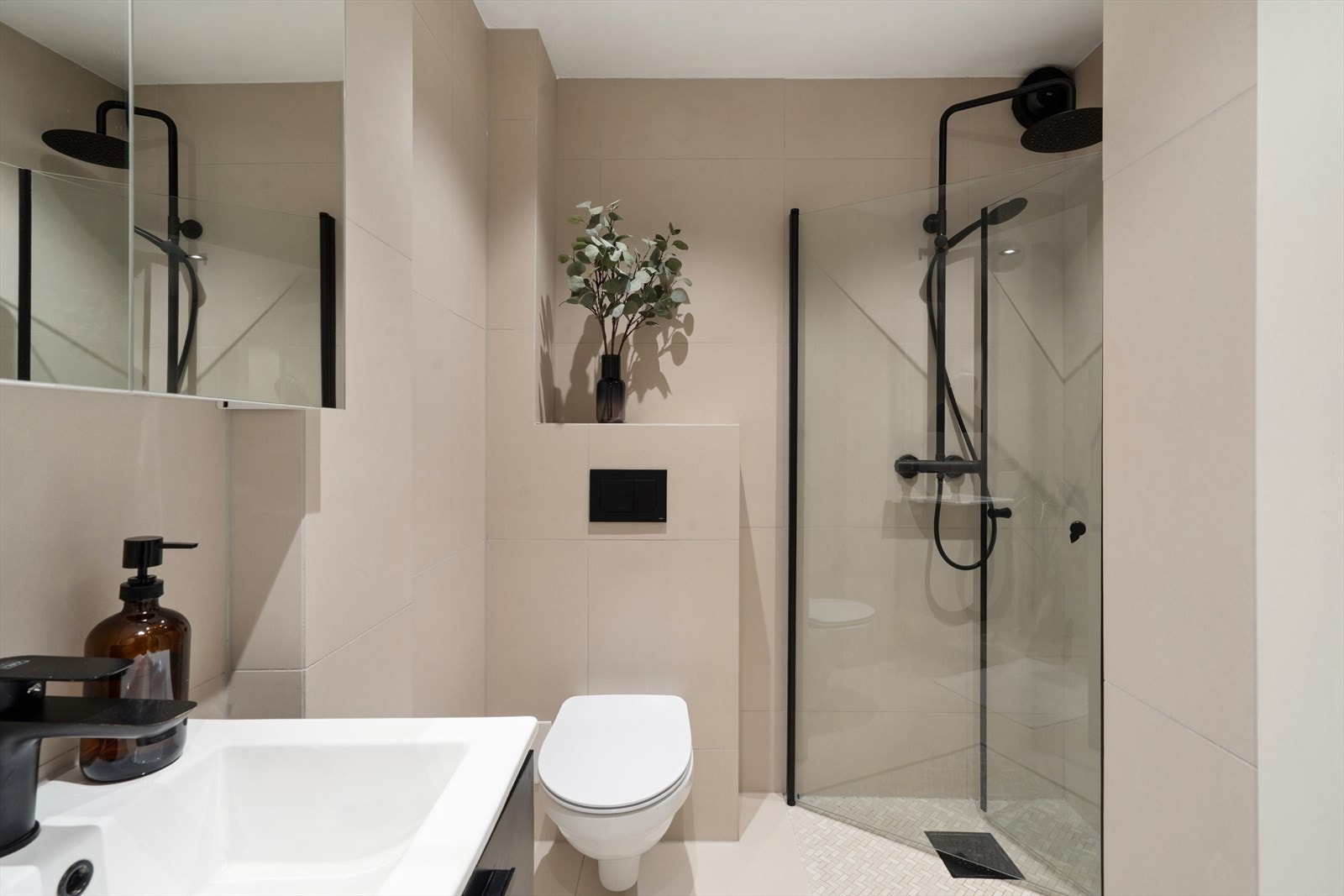 Romslig dusjsone etablert på gulv med glassavskjerming, takdusj og hånddusj i sort utførelse. Badet har varmekabler i gulv og opplegg for vaskemaskin. Galleribilde