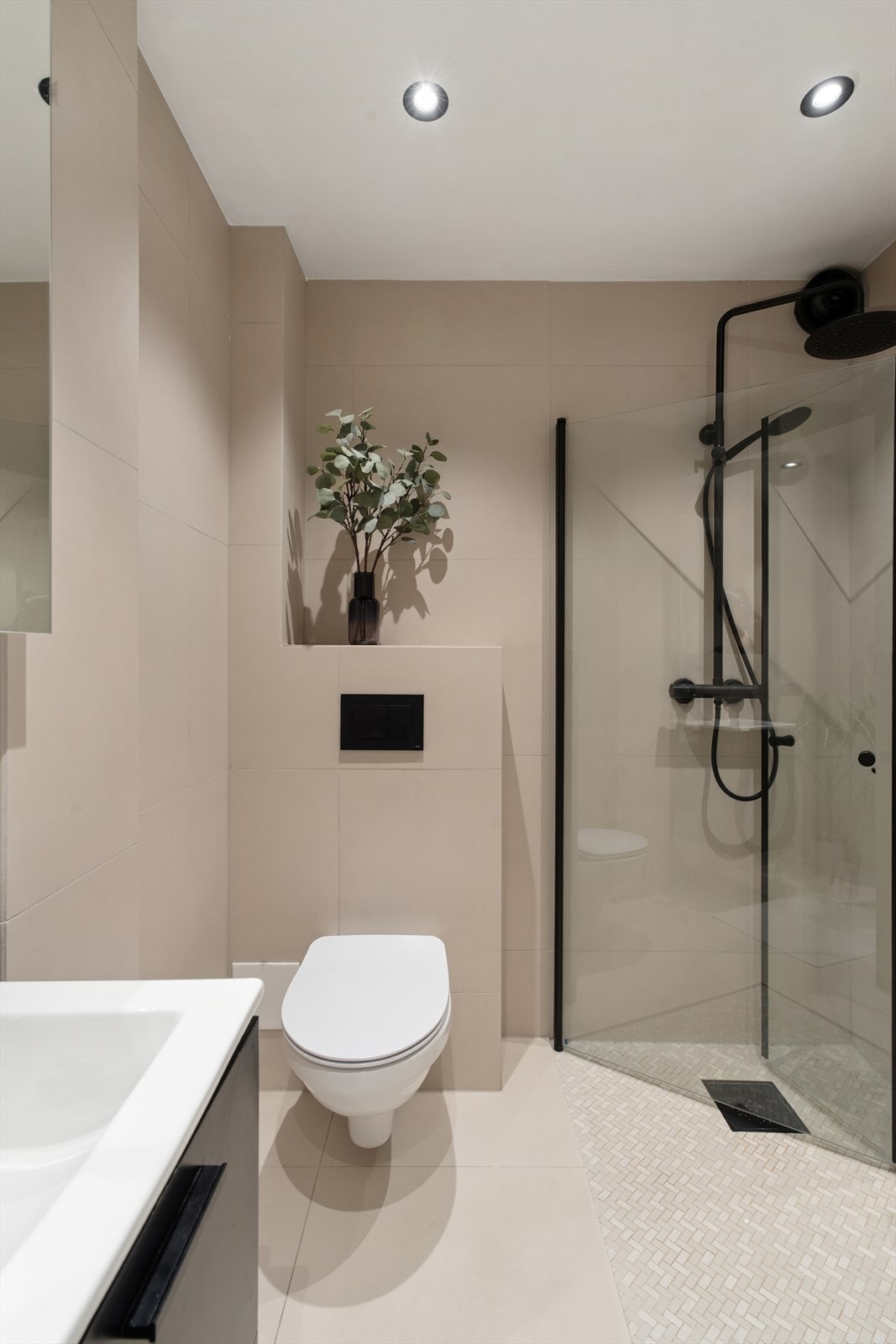 Delikat og moderne baderom oppgradert i 2022 med sandfargede fliser på vegger og gulv. Vegghengt toalett og dusjsone med sorte detaljer og glassvegger gir et stilrent uttrykk. Galleribilde
