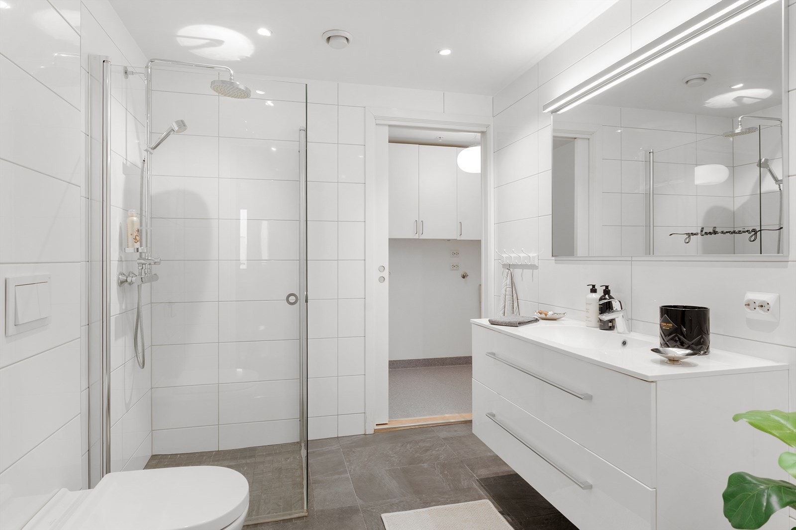 Leilighetens bad er innredet med dusjhjørne med vegger, veggmontert toalett, speil og baderomsinnredning med heldekkende servant. Galleribilde