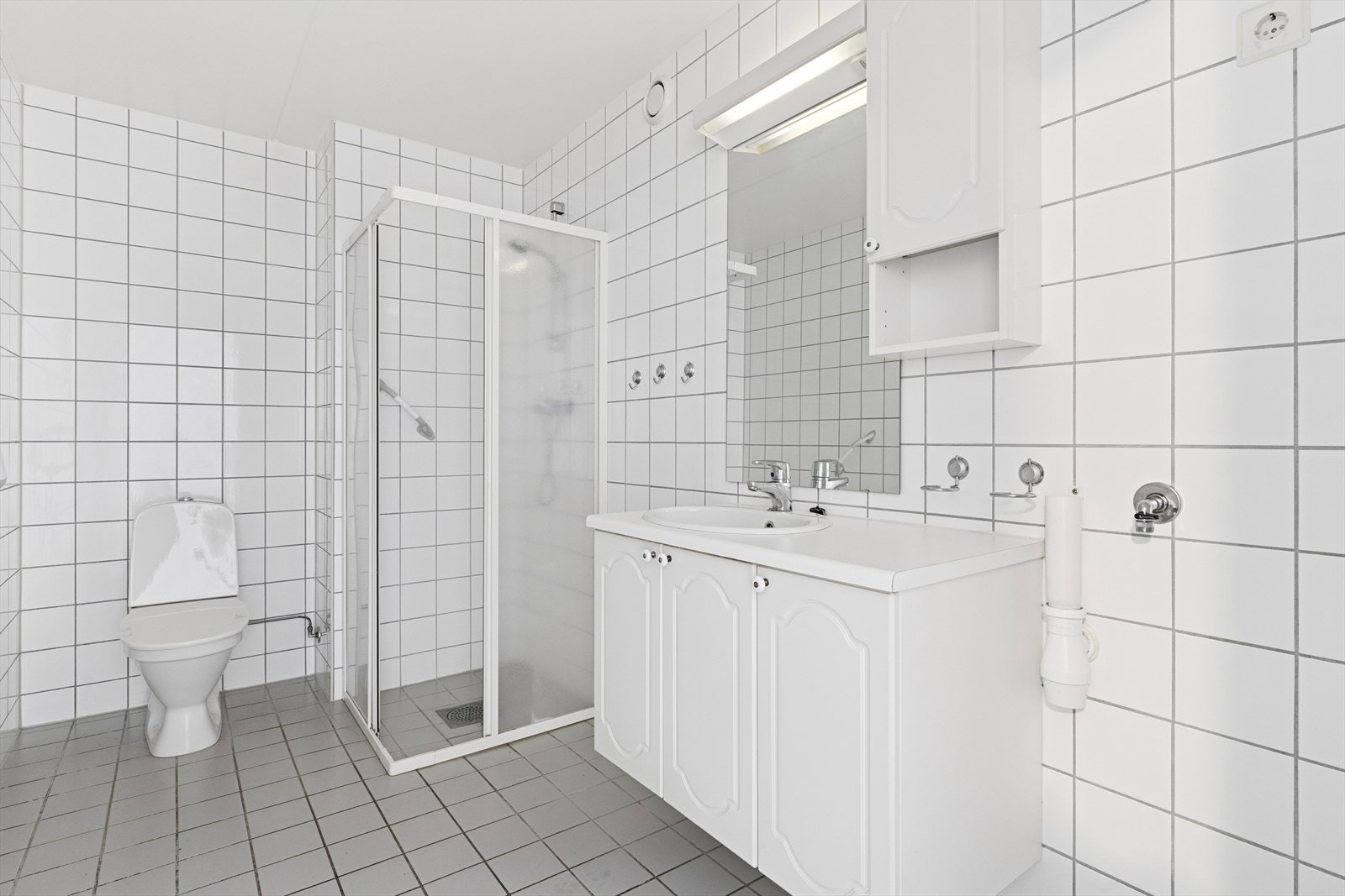 Badet er helfliset og utstyrt med gulvvarme, dusjhjørne med glassvegger og servant med underskap. Galleribilde