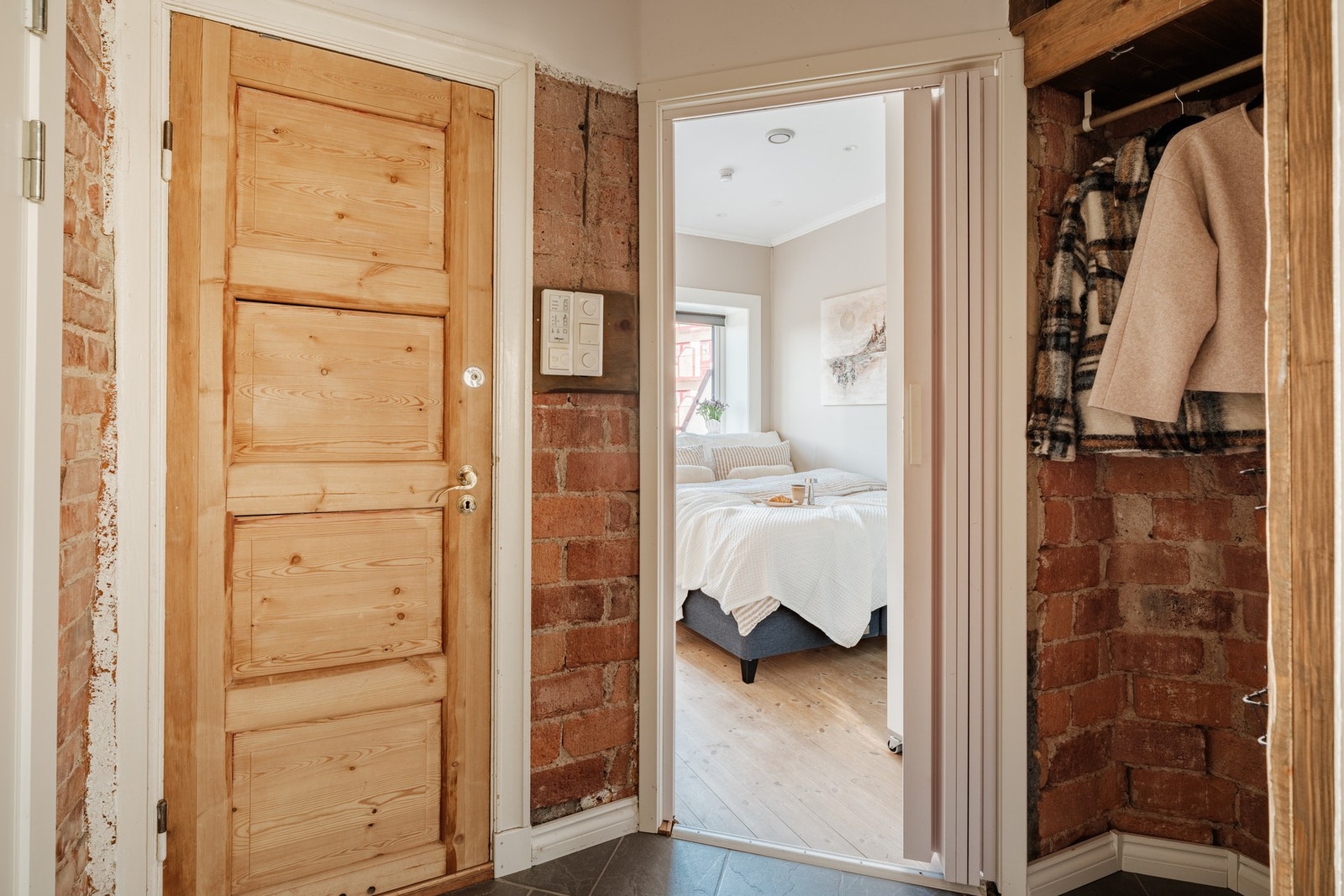 En innbydende gang med sjarmerende teglsteinsvegg og godt med oppheng til klær og sko Galleribilde