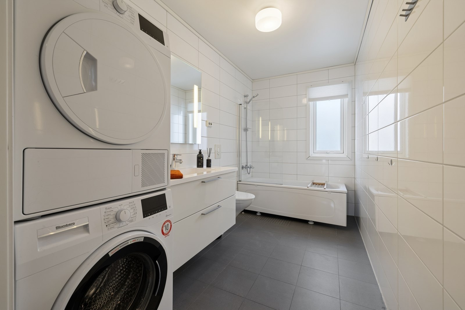 Badet er utstyrt med nedfelt servant, vegghengt toalett, badekar med glassplate og opplegg for vaskemaskin. Galleribilde