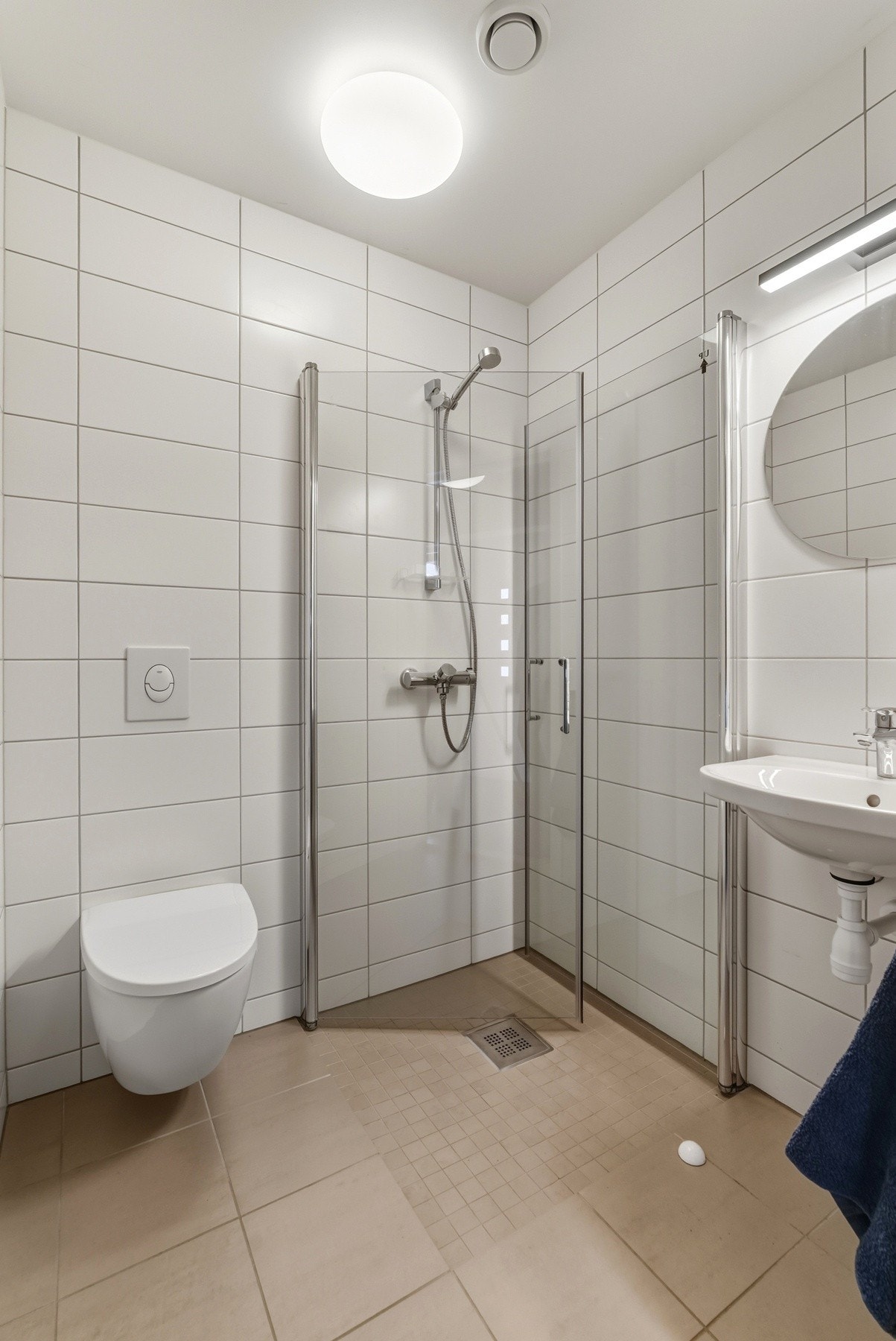 Tidløst og pent flislagt bad med varme i gulv. Vegghengt toalett, dusjhjørne med innfellbare vegger og servant med speil og lys ovenfor. Galleribilde