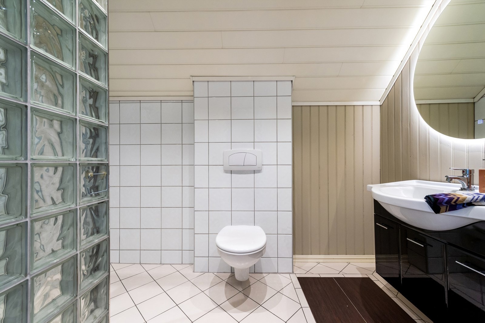 Badeet i 2. etasje er innredet med en servant nedfelt i innredningen, et veggmontert toalett og et dusjhjørne med glassbyggerstein. Galleribilde